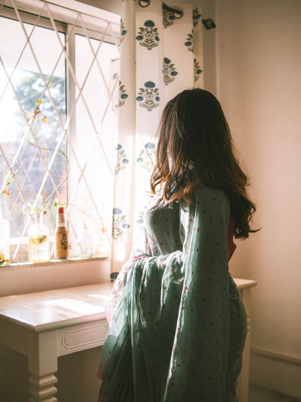 A woman in a saree looking out of a sunlit window